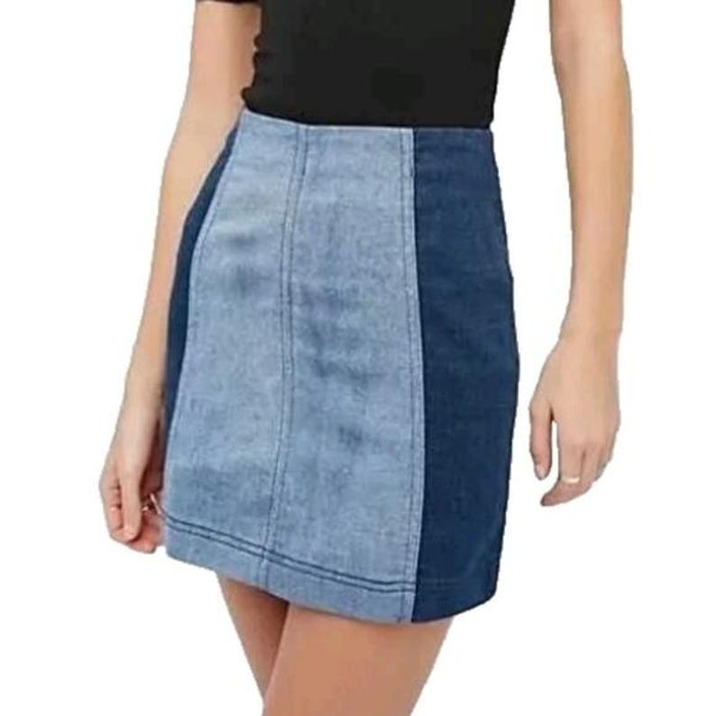 Puede incluir: Minifalda vaquera con dise&ntilde;o de bloques de color. La falda presenta un panel central azul claro flanqueado por paneles laterales azul oscuro. La falda tiene un dise&ntilde;o cl&aacute;sico de cinco bolsillos y un dobladillo recto.