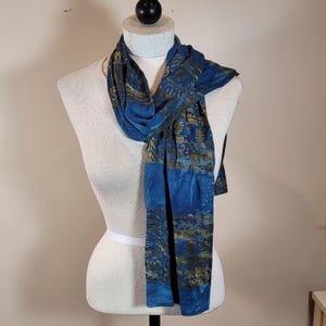 Può includere: Una sciarpa blu e oro con un design geometrico. La sciarpa è realizzata in un tessuto morbido e leggero, perfetta per aggiungere un tocco di stile a qualsiasi outfit.