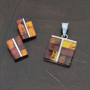 May include: A set of amber and silver earrings and a pendant necklace. The amber is a mix of brown, orange, and yellow colors. The silver is a shiny metal.