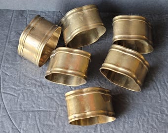 Può includere: Set di sei anelli per tovaglioli in metallo dorato. Gli anelli sono di forma ovale con un bordo leggermente ondulato.
