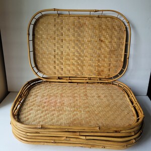 Puede incluir: Un juego de cuatro bandejas de bambú tejido, apiladas una encima de la otra. Las bandejas son rectangulares y tienen un color marrón natural.