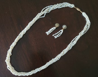 May include: A white pearl necklace and matching earrings. The necklace is made of multiple strands of pearls and has a gold clasp. The earrings are also made of pearls and have gold posts.