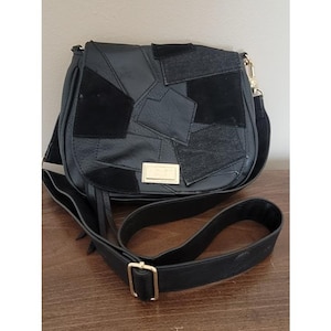 May include: A black crossbody bag featuring a patchwork design of smooth and textured panels. The front flap includes a rectangular gold-tone metal plaque. The bag has an adjustable black shoulder strap with gold-tone hardware and side tassels.