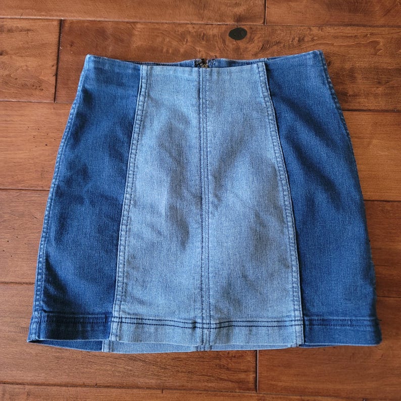 Puede incluir: Minifalda vaquera con dise&ntilde;o de bloques de color. La falda presenta un panel central azul claro flanqueado por paneles laterales azul oscuro. La falda tiene cierre de cremallera y est&aacute; hecha de tejido vaquero.