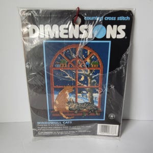 Può includere: Un kit Dimensions a punto croce contato intitolato "Windowsill Cats". Il kit presenta un disegno a punto croce di due gatti che guardano fuori da una finestra una scena notturna. La dimensione del telaio è di 13 cm x 18 cm.