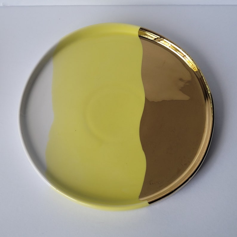Puede incluir: Un plato redondo de cer&aacute;mica con un dise&ntilde;o amarillo y dorado. El plato est&aacute; dividido en dos, con un lado amarillo y el otro dorado. El lado dorado tiene un acabado brillante y met&aacute;lico.