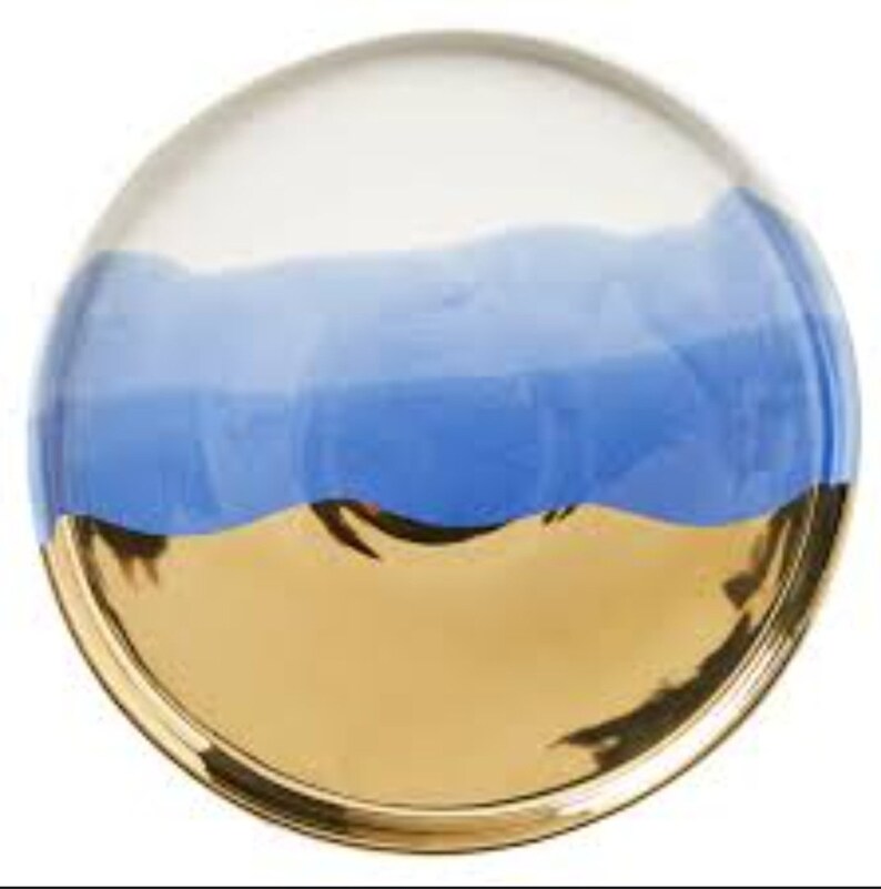 Puede incluir: Un plato redondo de cer&aacute;mica con un dise&ntilde;o blanco, azul claro y dorado. El plato tiene un efecto degradado ondulado con una capa superior azul claro que se funde en una capa azul m&aacute;s oscura, y una capa inferior dorada.