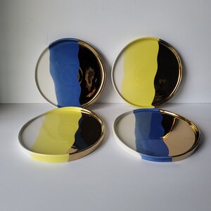 Puede incluir: Cuatro platos de cer&aacute;mica con un dise&ntilde;o moderno. Cada plato presenta una combinaci&oacute;n de colores diferente de amarillo, azul y dorado.