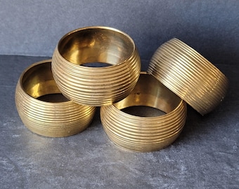 Può includere: Set di quattro anelli tovagliolo in ottone dorato con design rigato.