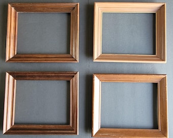May include: Four rectangular wooden picture frames in shades of brown and tan. The frames are empty, with a simple, classic design. The arrangement is on a grey surface, showcasing the different wood tones.