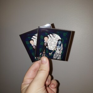 May include: Two stickers featuring a stained glass style illustration of Jack Skellington and Sally from the Nightmare Before Christmas movie. The stickers are on a white background.