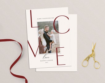 May include: A Valentine's Day card featuring a photograph of a family of three. The card displays the word "LOVE" in large, bold, red lettering. The text "Happy Valentine's Day" is printed at the top of the card. The text "love" is written in cursive below the photo. The text "Danny & Ellie 2021" is printed below the cursive text.