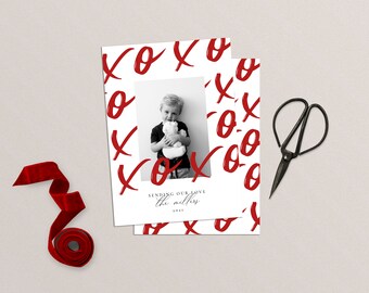 May include: A white Christmas card with a red and white XOXO pattern. A black and white photo of a child holding a stuffed animal is in the centre of the card. The text "Sending our love the Millers 2023" is printed on the card.