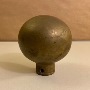 May include: A brass ball finial with a small hole in the bottom. The finial is a decorative element often used on furniture or other objects.