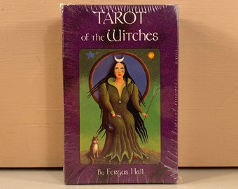 May include: A tarot card deck titled "Tarot of the Witches" in a purple box. The box features an illustration of a woman with long black hair, a crescent moon, and a cat. The artist's name, Fergus Hall, is printed at the bottom.
