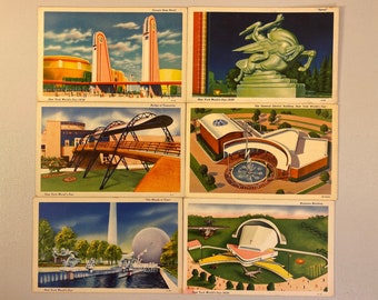 May include: Five vintage postcards depicting different buildings and attractions from the 1939 New York World's Fair. The postcards feature images of the Trylon and Perisphere, the General Motors Building, the Bridge of Tomorrow, the  'The World of Tomorrow' exhibit, and the  'Amusement Building'.