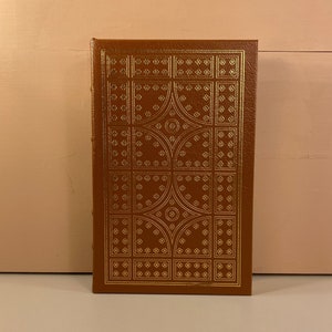 May include: A brown leather-bound book with a gold-colored geometric pattern on the cover.