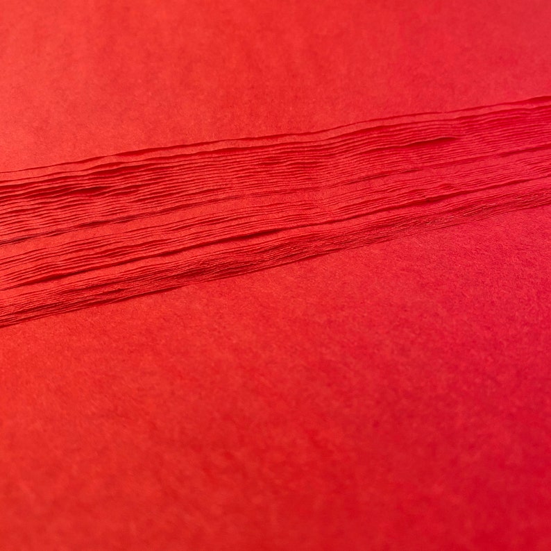 Pu&ograve; includere: Un mucchio di carta velina rossa. La carta &egrave; piegata in una pila ordinata, con i bordi di ogni foglio visibili.