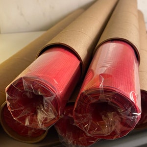 Pu&ograve; includere: Primo piano di tre rotoli di carta rossa avvolti in plastica trasparente e tubi di cartone marrone.