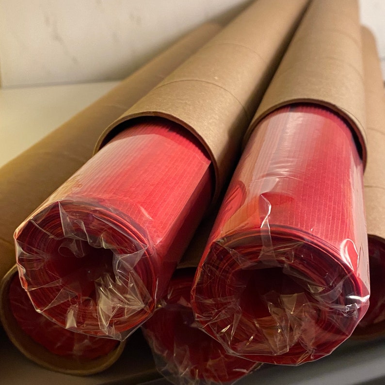 Pu&ograve; includere: Primo piano di tre rotoli di carta rossa avvolti in plastica trasparente e tubi di cartone marrone.