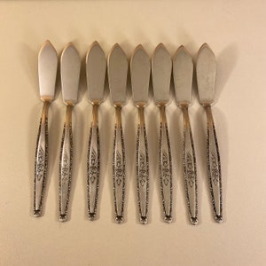 May include: Eight silver butter knives with floral designs on the handles.
