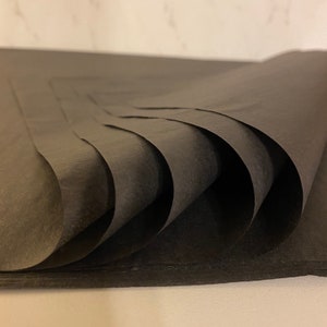 May include: A stack of black tissue paper, folded and layered, creating a textured and abstract pattern.