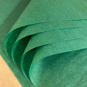Puede incluir: Papel de seda verde doblado en forma de abanico. El papel tiene una superficie texturizada.