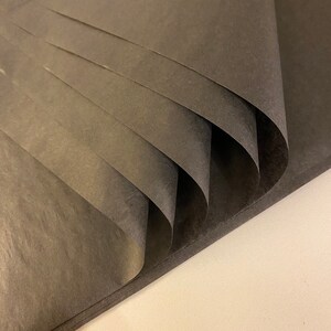 May include: Black tissue paper folded in a fan shape. The paper has a subtle texture and is a dark charcoal color.