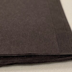 May include: A stack of black paper sheets. The paper has a textured surface.