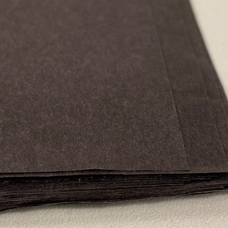 May include: A stack of black paper sheets. The paper has a textured surface.