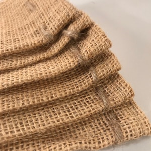May include: A stack of four brown burlap bags with a woven texture. The bags are folded over at the top and have a sewn edge.
