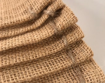 May include: A stack of four brown burlap bags with a woven texture. The bags are folded over at the top and have a sewn edge.