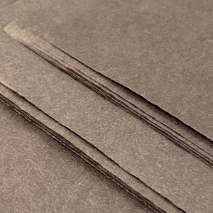 May include: A stack of dark gray paper sheets with a textured surface.