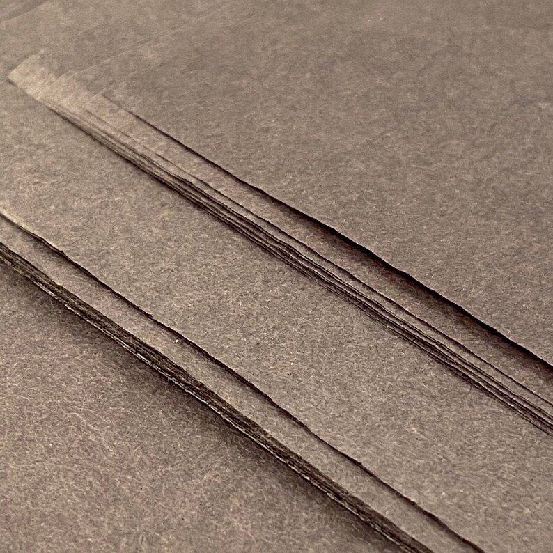 May include: A stack of dark gray paper sheets with a textured surface.