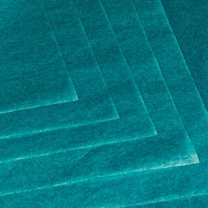 May include: A stack of teal-colored felt sheets, arranged in a layered pattern. The sheets have a slightly textured surface and are angled to create a geometric design. The color is a vibrant, saturated teal.