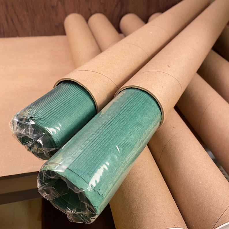 Puede incluir: Varios tubos de cart&oacute;n marr&oacute;n con rollos de papel verde en su interior. Los tubos est&aacute;n apilados unos sobre otros.