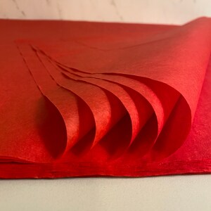 Pu&ograve; includere: Un pacco di carta velina rossa, piegato a ventaglio, con una texture liscia.