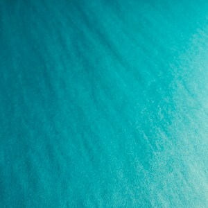 May include: A close-up shot of a textured, teal-colored surface. The surface has a subtle, rippled pattern, with variations in tone creating depth and visual interest. The overall effect is a smooth, flowing appearance.