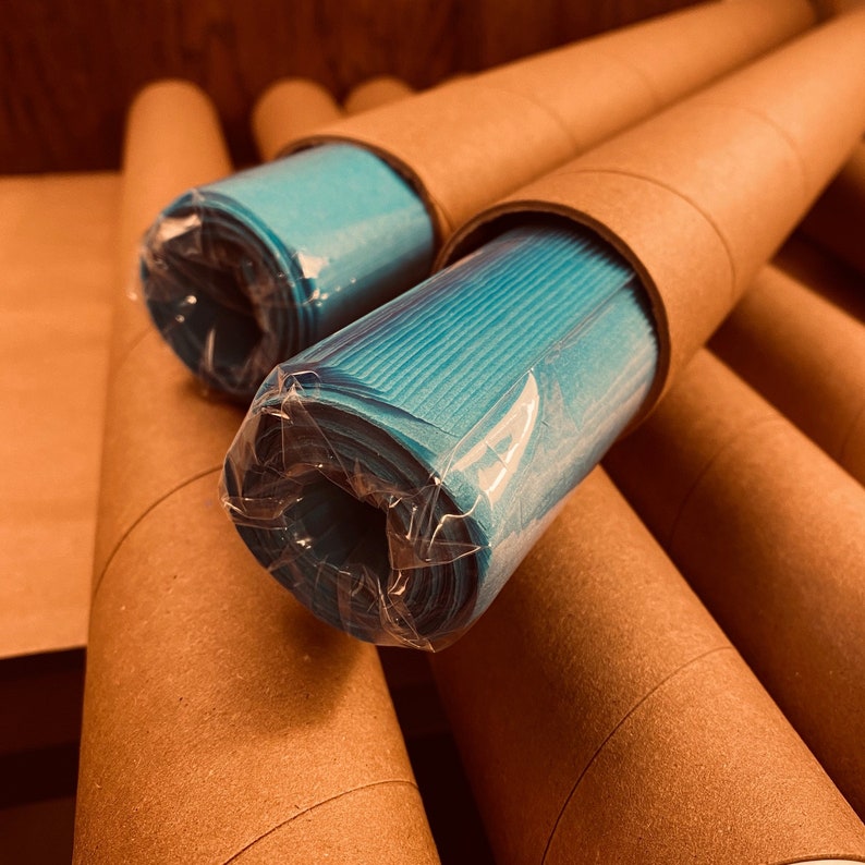 May include: Several rolls of turquoise paper are visible, each encased in a brown cardboard tube and wrapped in clear plastic. The tubes are arranged at various angles, creating a layered effect. The paper appears to be a solid color.
