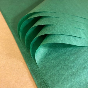 Puede incluir: Una pila de papel de seda verde, doblado y enrollado, con una superficie texturizada. El papel es de un color verde intenso y rico.