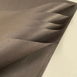 May include: A stack of dark gray tissue paper, folded and layered, creating a soft, textured look.