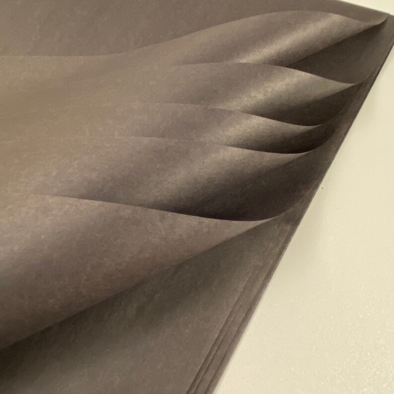 May include: A stack of dark gray tissue paper, folded and layered, creating a soft, textured look.