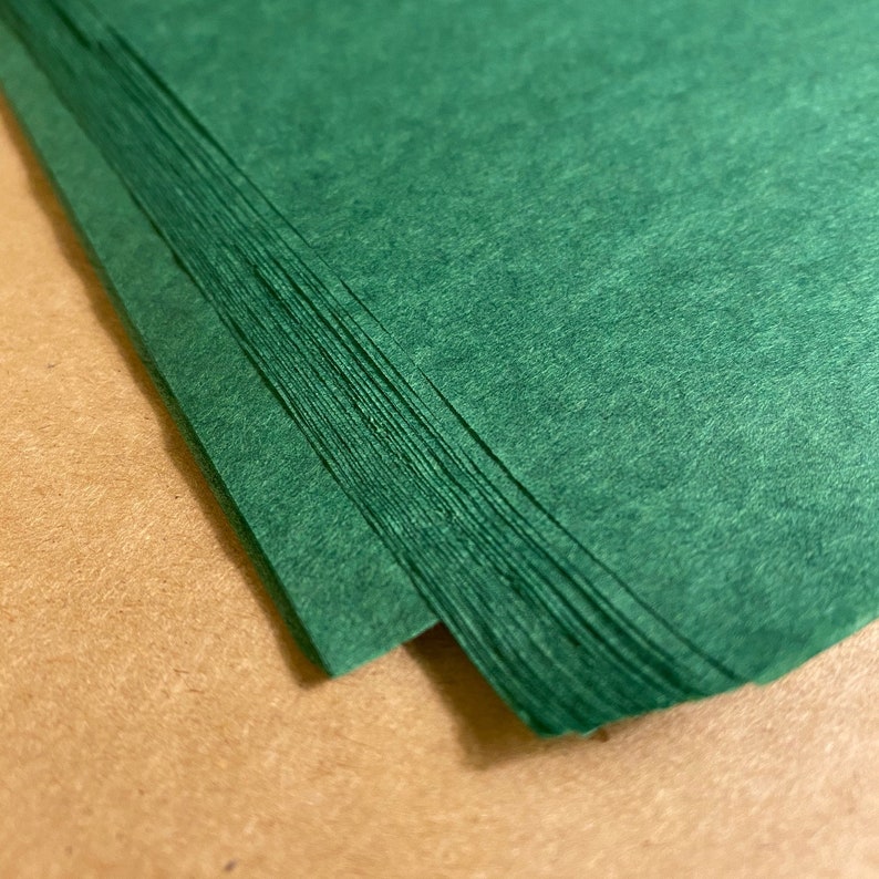 Puede incluir: Una pila de hojas de papel verde, dobladas por la mitad, con una superficie texturizada.