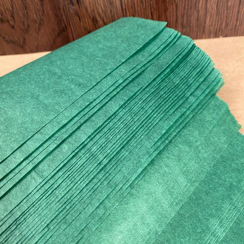 Puede incluir: Una pila de papel de seda verde. El papel est&aacute; doblado y superpuesto, creando una superficie texturizada.