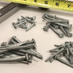 May include: Four piles of silver-colored nails of different sizes and shapes. The nails are arranged in a random pattern on a white surface.