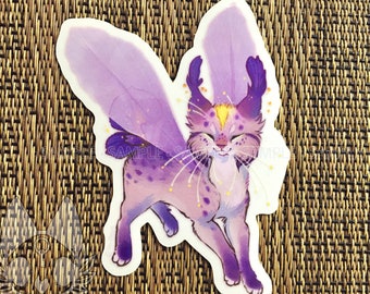 May include: A sticker featuring a whimsical creature with purple fur, large feathery wings, and a serene expression. The design includes a yellow gem on its forehead and sparkling accents. The text "SAMPLE" is visible on the sticker.