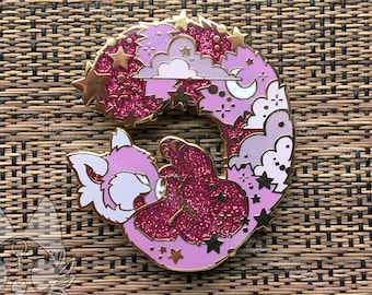 May include: Pink enamel pin of a red panda curled up sleeping with a pink, white, and blue starry sky background.