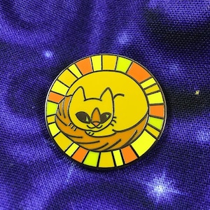 May include: A yellow enamel pin with a stylized orange cat curled up inside a sun with orange, yellow, and green rays.