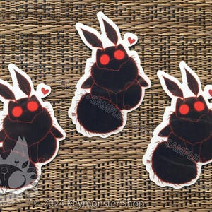 May include: Three black and red moth stickers with a fuzzy texture and red eyes. The stickers have the word "SAMPLE" printed on them.