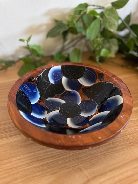 A hand-carved wooden catch-all bowl with cobalt blue and black resin flowers inlaid into the wood — the color contrast makes it look like jewelry for your countertop.